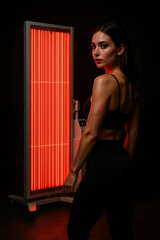 Woman standing beside the Zenapura GlowLift Red Light Therapy Panel in a dark setting, showcasing full body red and near infrared light for skin rejuvenation and wellness.